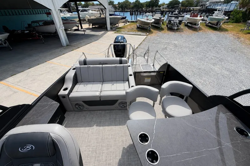 Slide: The Image of 2026 Barletta Lusso 25UE pontoon boat interior with seating and table, docked near other boats. - 17