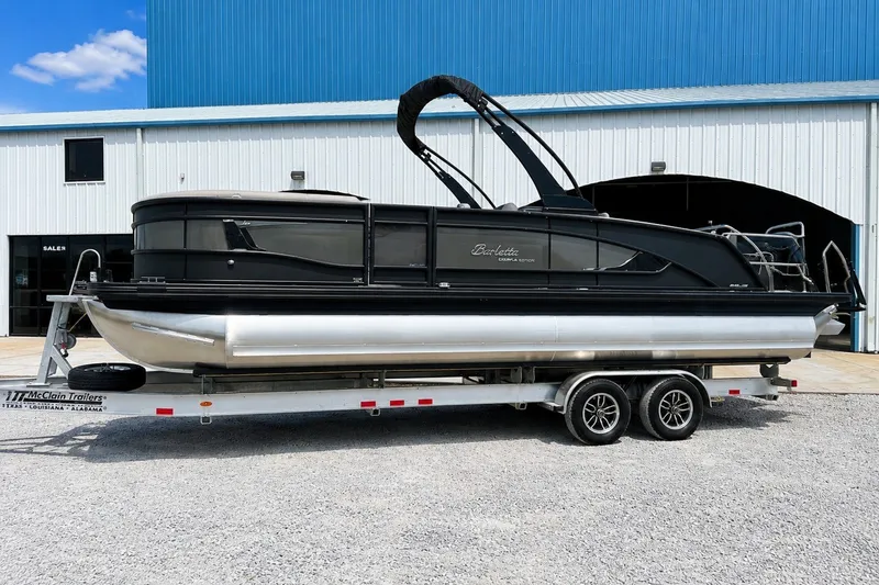 The Image of 2026 Barletta Lusso 25UE pontoon boat on trailer, parked outside a blue building. - 0