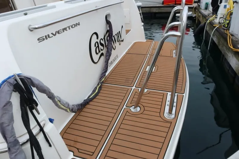 Slide: The Image of 2000 Silverton 330 Sport Bridge boat docked, featuring teak swim platform and stainless steel ladder. - 17