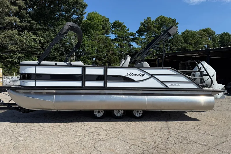Slide: The Image of 2026 Bentley Pontoons Legacy 223 Swingback pontoon boat on a trailer, parked outdoors. - 2