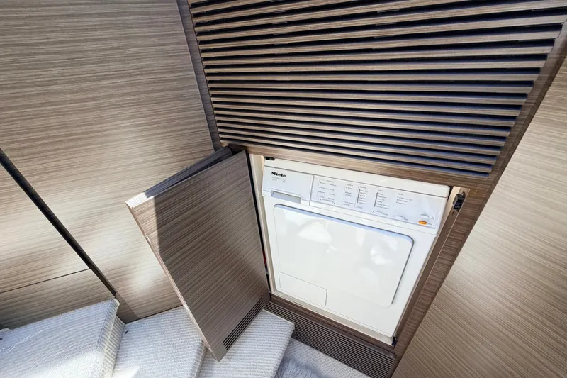 Slide: The Image of Laundry area with Miele appliance on 2014 Azimut 64 yacht, featuring sleek wooden paneling. - 23