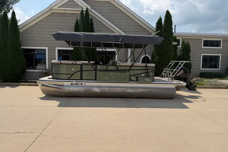 Slide: The Image of 2025 Crest Classic 200 pontoon boat with canopy, parked outside a building. - 1