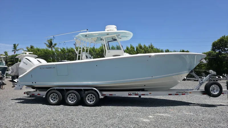 Slide: The Image of A 2025 Cobia 301 Center Console boat on a trailer, surrounded by trees and clear sky. - 3
