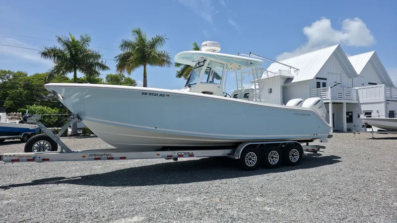 Slide: The Image of A 2025 Cobia 301 Center Console boat on a trailer in front of a white building. - 2