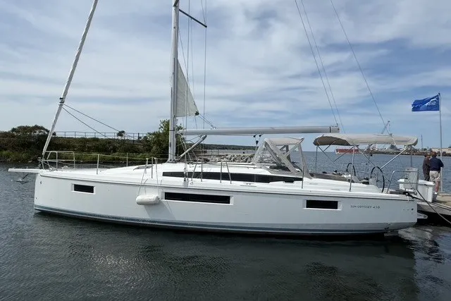 Slide: The Image of 2022 Jeanneau Sun Odyssey 410 sailboat docked on calm water under a cloudy sky. - 1