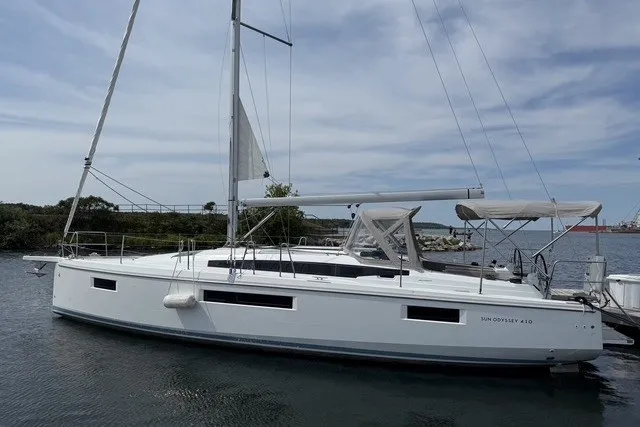The Image of 2022 Jeanneau Sun Odyssey 410 sailboat docked on calm water under a cloudy sky. - 0