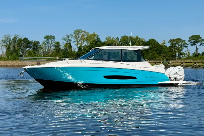 Slide: The Image of 2023 Regal 36 XO boat cruising on a calm lake with a scenic forest backdrop. - 12