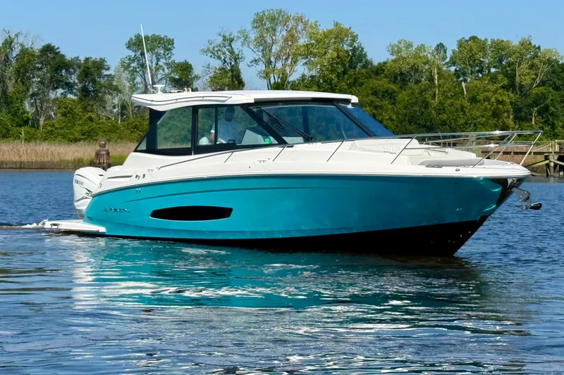 Slide: The Image of 2023 Regal 36 XO boat cruising on a serene lake with lush greenery. - 7