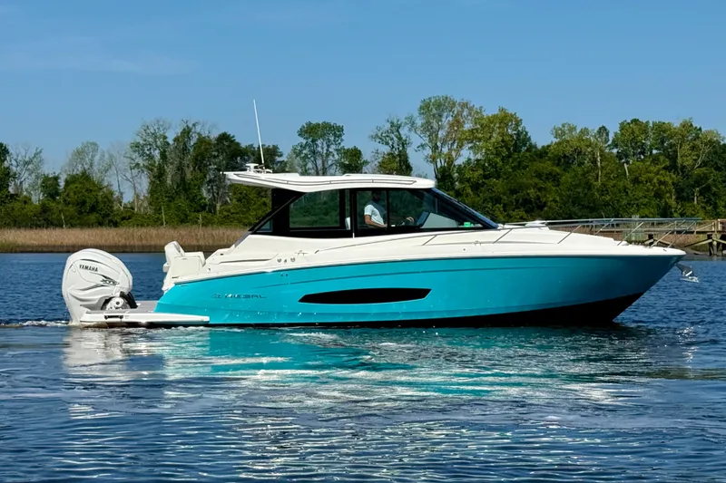 Slide: The Image of 2023 Regal 36 XO boat cruising on a calm lake with lush green trees. - 6