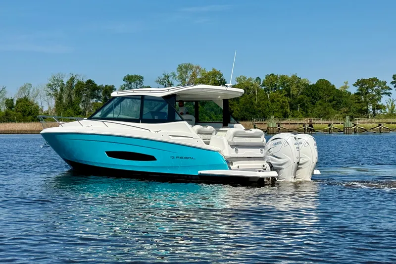 Slide: The Image of 2023 Regal 36 XO boat on calm water with lush green shoreline. - 1