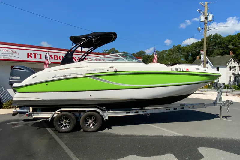 The Image of 2013 Hurricane SunDeck 2400 OB boat on trailer, vibrant green and white design. - 1
