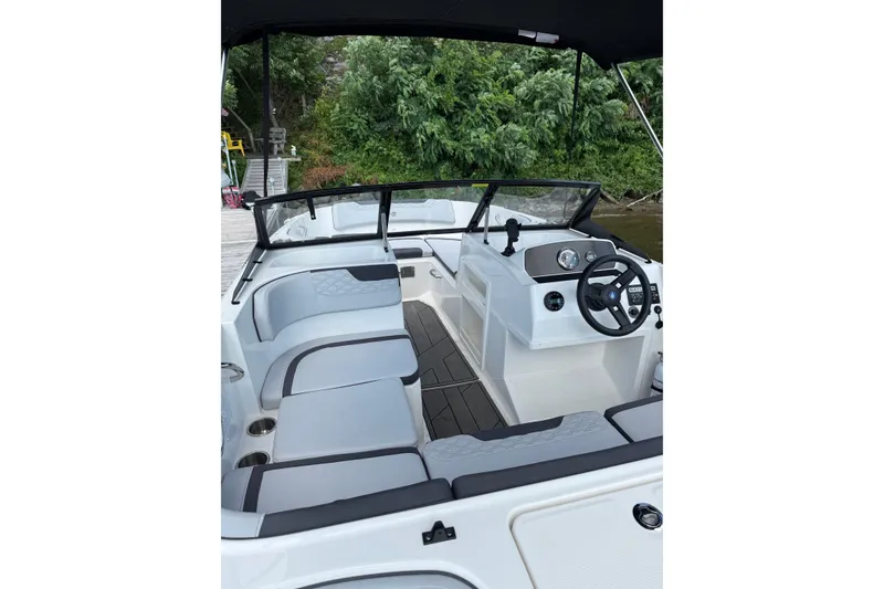 Slide: The Image of 2024 Bayliner Element M17 boat interior with seating and steering wheel, docked by lush greenery. - 8