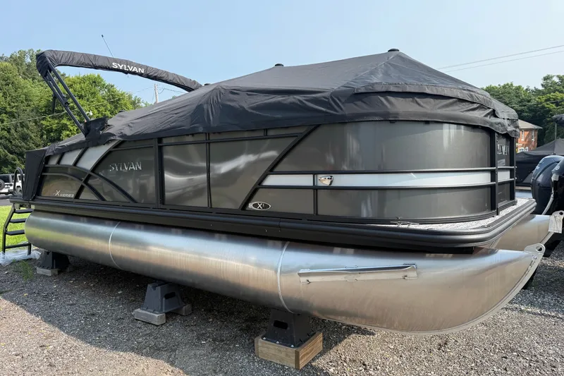 Slide: The Image of 2026 Sylvan X1 CLZ DH pontoon boat with cover, parked on gravel. - 27