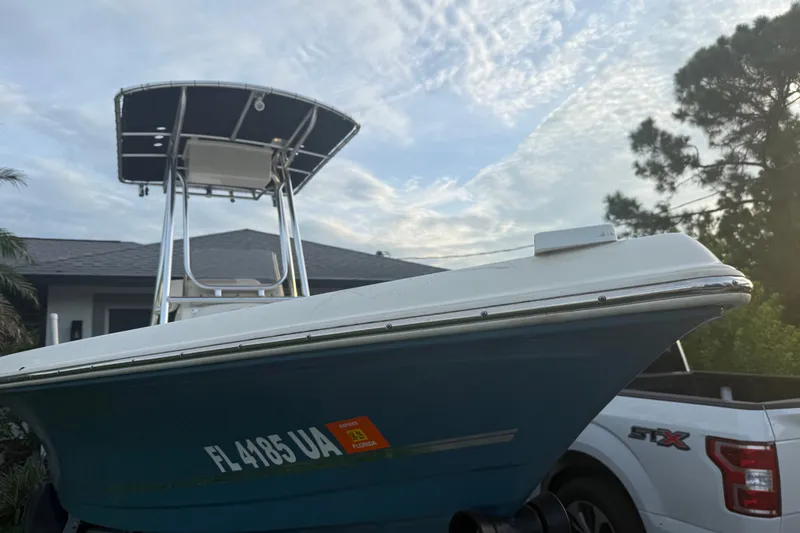Slide: The Image of 2025 Bulls Bay 2200 XS boat with T-top, parked beside a white truck, under a cloudy sky. - 2