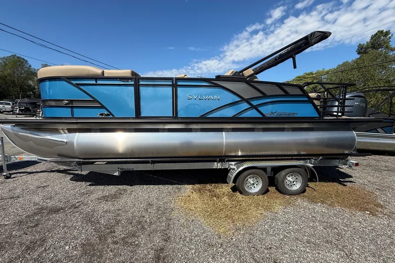 The Image of 2026 Sylvan X-3 CLZ DH pontoon boat on trailer, blue and silver design, sunny day. - 1