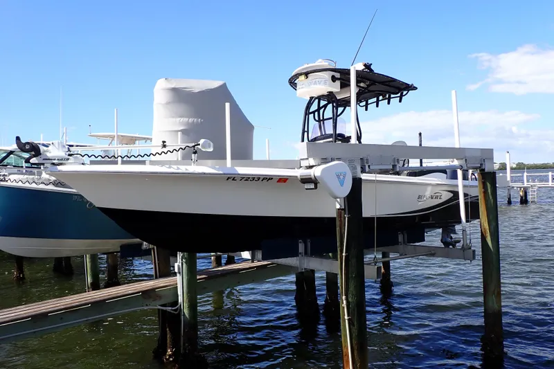 The Image of 2015 Blue Wave 2400 PureBay boat on lift, docked by the water under a clear blue sky. - 0