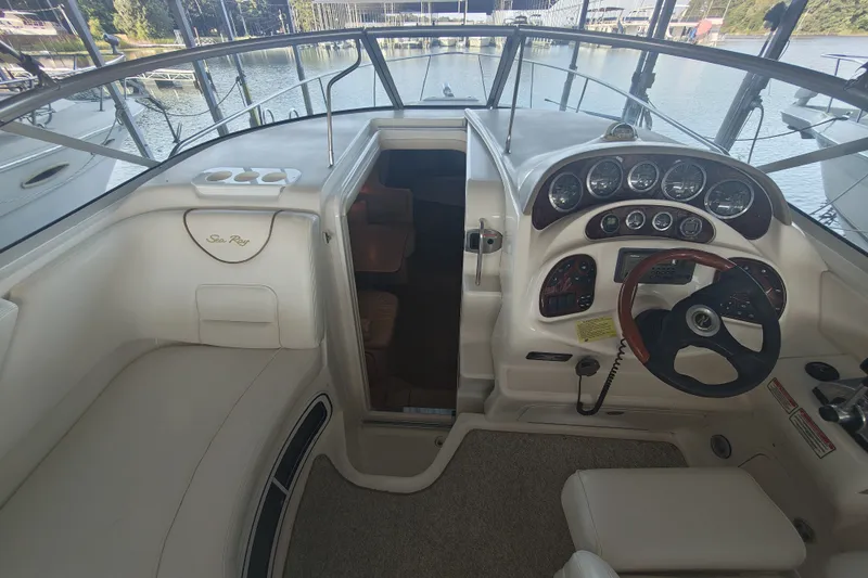 Slide: The Image of 2002 Sea Ray Sundancer 280 cockpit with steering wheel, gauges, and seating, docked by the water. - 8