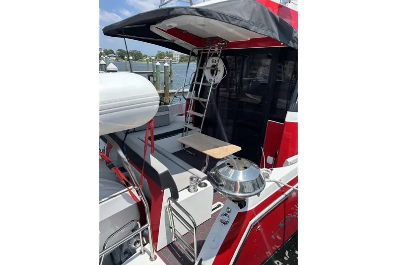 Slide: The Image of 2024 Jeanneau NC Weekender 1095 Fly, red exterior, docked with outdoor seating and grill. - 13