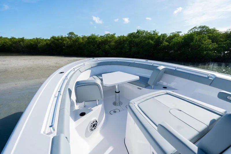 Slide: The Image of 2027 Sportsman Open 232 Center Console boat interior with seating and table, near shoreline. - 9