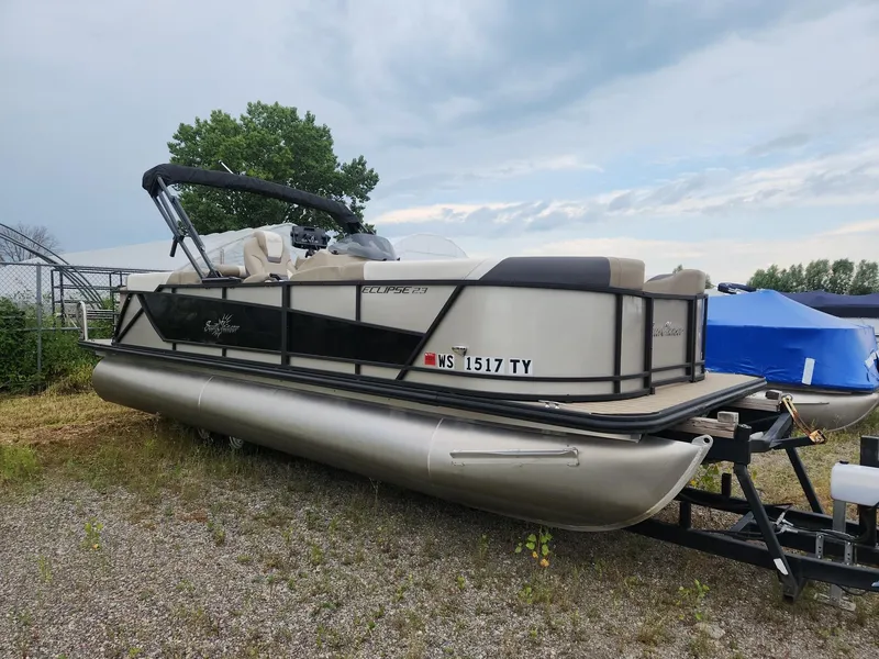 Slide: The Image of A 2023 SunChaser Eclipse 8523 LR DH pontoon boat on a trailer in a gravel lot. - 2