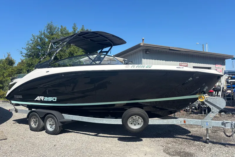 The Image of 2023 Yamaha Boats AR250 on trailer, black and white design, parked outdoors. - 1