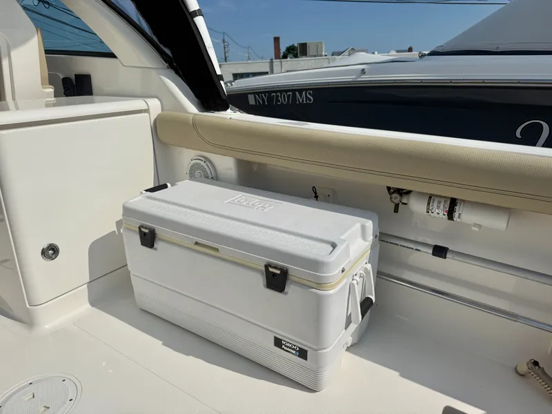 Slide: The Image of The image shows the cockpit of a 2019 Pursuit DC 265 Dual Console boat. A white cooler sits on the floor, surrounded by beige upholstery and a speaker. - 11
