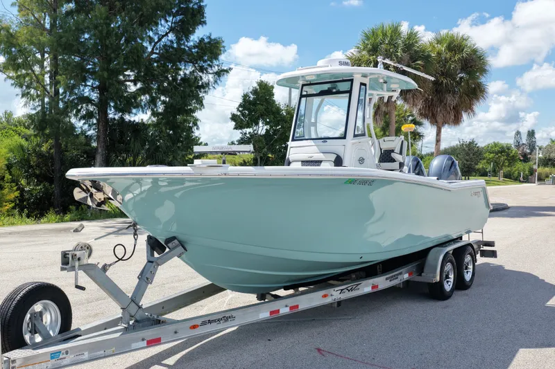 Slide: The Image of 2021 Tidewater 256 CC Adventure boat on trailer, parked outdoors under clear sky. - 2