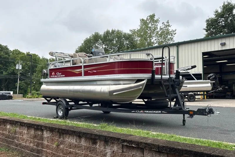 Slide: The Image of 2024 Sun Tracker Bass Buggy 18 DLX pontoon boat on trailer outside a garage. - 32