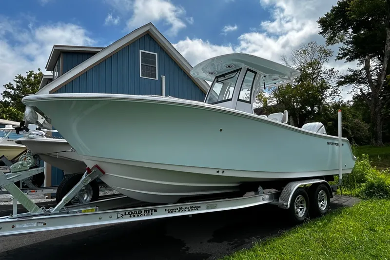 The Image of 2026 Sportsman Open 232 Center Console boat on trailer, parked near blue building. - 1