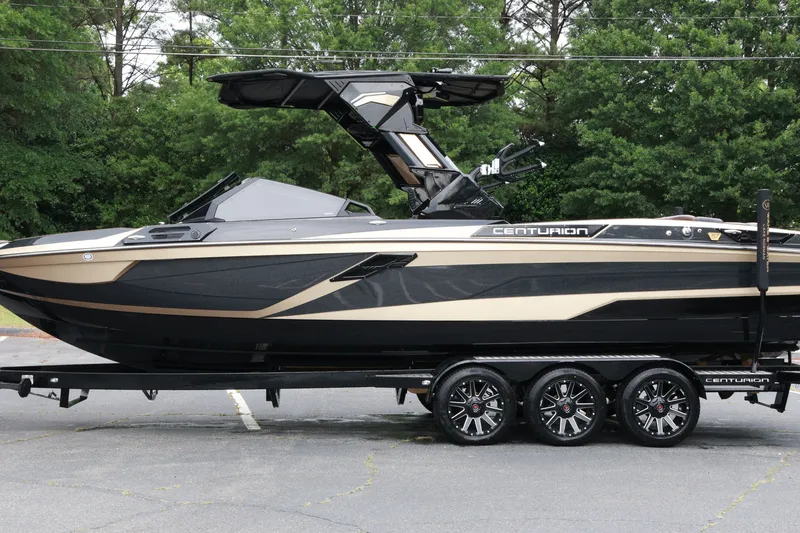 Slide: The Image of 2026 Centurion Ri265 boat on trailer, sleek black and gold design, parked outdoors. - 6