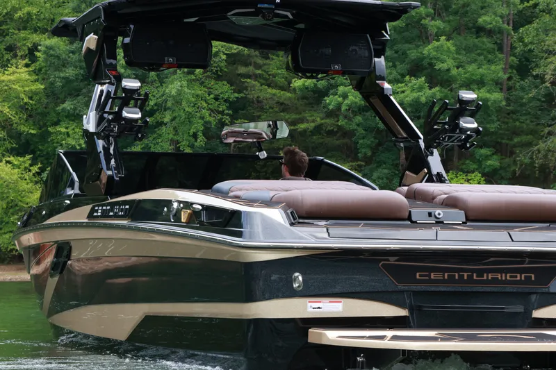 Slide: The Image of 2026 Centurion Ri265 boat cruising on a lake surrounded by lush greenery. - 2
