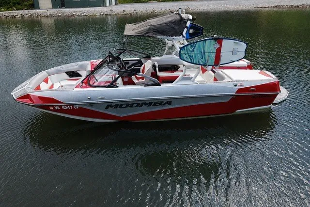 The Image of 2021 Moomba Kaiyen boat in water, red and white design, with wakeboard rack. - 2