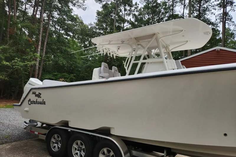 Slide: The Image of 2024 SeaVee 322Z boat on trailer, surrounded by trees and a red building. - 2