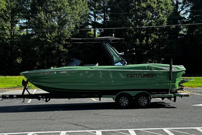 Slide: The Image of 2026 Centurion Nv243 boat on trailer, parked outdoors with lush trees in background. - 26