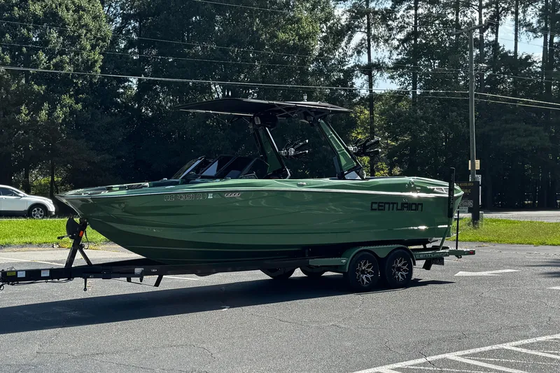 Slide: The Image of Green 2026 Centurion Nv243 boat on trailer, parked outdoors with trees in background. - 25
