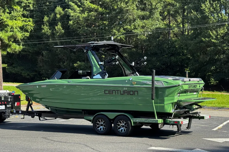 Slide: The Image of Green 2026 Centurion Nv243 boat on trailer, parked outdoors with lush trees in background. - 27