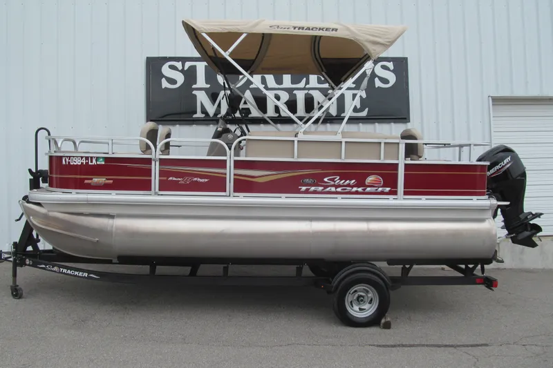 The Image of 2023 Sun Tracker Bass Buggy 18 DLX pontoon boat with canopy, parked on trailer. - 0
