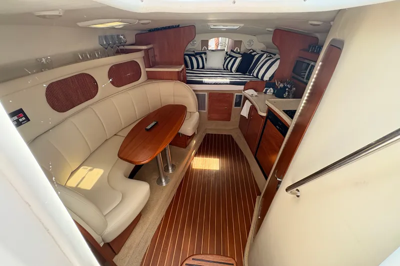 Slide: The Image of 2008 Rinker 320 Express Cruiser interior with elegant seating, wooden table, and cozy sleeping area. - 17