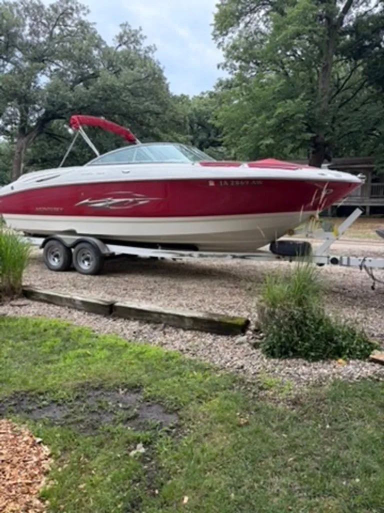 The Image of A red 2006 Monterey 248LS Montura Bowrider on a trailer, surrounded by trees. - 0