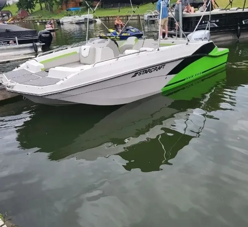 The Image of A white and green 2023 Starcraft SVX 191 OB boat docked at a calm pier. - 1