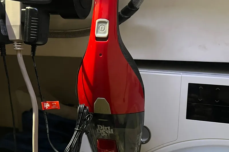 Slide: The Image of Red Dirt Devil handheld vacuum cleaner plugged in, next to a washing machine. - 70