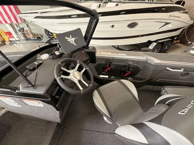 Slide: The Image of The image shows the cockpit of a 2027 Lund 1875 Tyee SS boat. It features a modern helm with a sleek steering wheel and digital display. Other boats are visible in the background. - 8