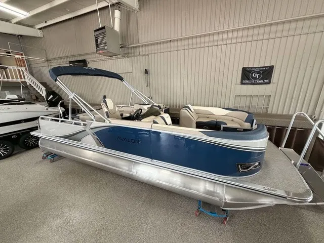 The Image of A blue Avalon LSZ 2385 VRB pontoon boat from 2027 is indoors. It features a canopy and comfortable seating. - 1