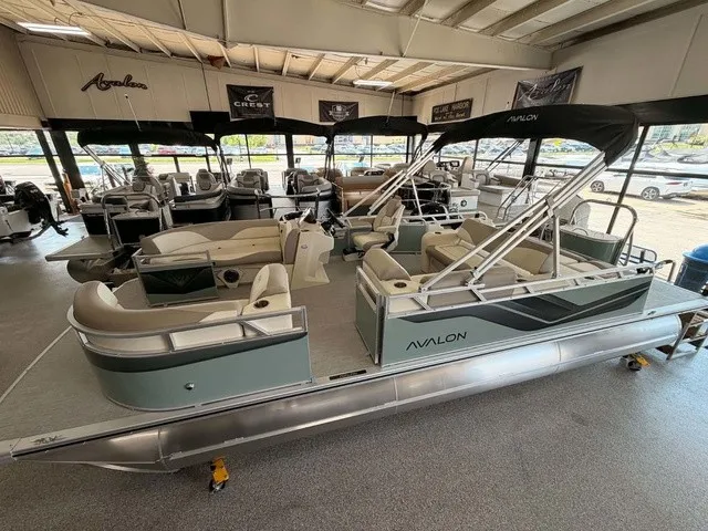 The Image of An Avalon VEN 23E85 VRB pontoon boat from 2027 is in a showroom with several other boats. - 1
