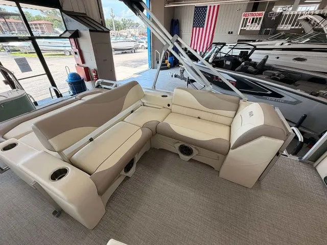 Slide: The Image of The image shows the interior of a 2027 Avalon VEN 23E85 VRB. It features beige and cream seating with cup holders and speakers. Other boats and an American flag are visible in the background. - 10