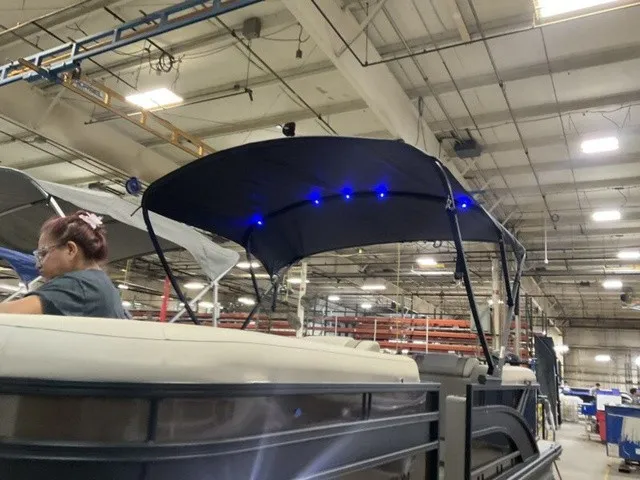Slide: The Image of A 2027 Bennington S Quad Bench 22 SSR Tritoon with a lit Bimini top in a warehouse. - 17