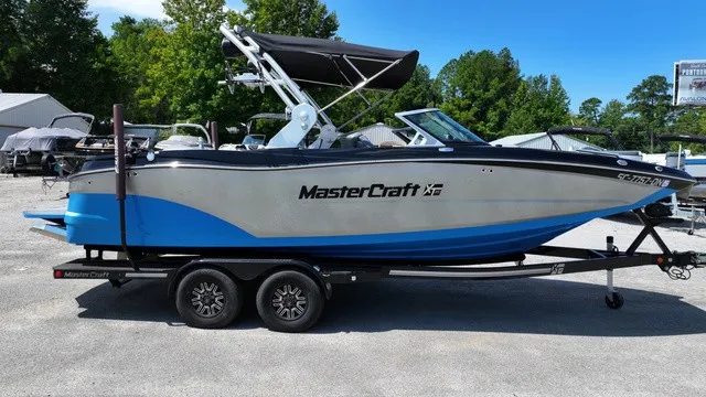 Slide: The Image of 2019 MasterCraft XT22 on a trailer, featuring a blue and gray hull, parked outdoors. - 2