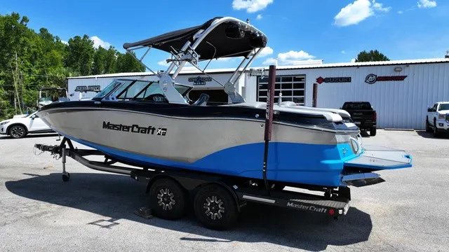 Slide: The Image of A 2019 MasterCraft XT22 boat on a trailer in a parking lot. It features a blue and white design with a black bimini top. - 9