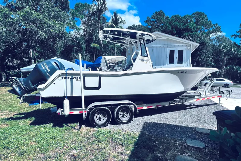 Slide: The Image of 2021 Tidewater 256 CC Adventure boat on trailer, parked outdoors with trees and a building nearby. - 30