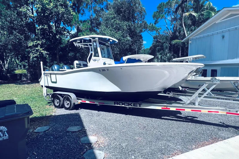 Slide: The Image of 2021 Tidewater 256 CC Adventure boat on trailer, parked outdoors near trees and a building. - 31